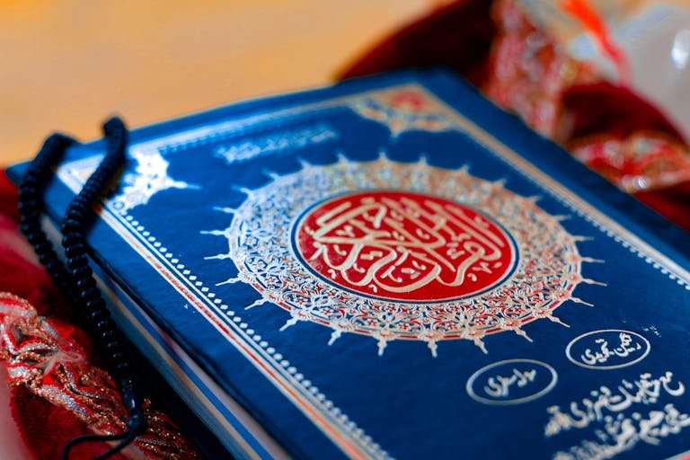 A close-up photograph of the Holy Quran with prayer beads, depicting Islamic spirituality.